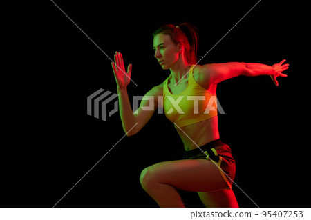 Dynamic portrait of young sportive woman training, running isolated on dark background in neon light. Competition, sport, fitness, speed and energy concept. Dynamic portrait of young sportive woman training, running isolated on dark background in neon light. Competition, sport, fitness, speed and energy concept. 95407253