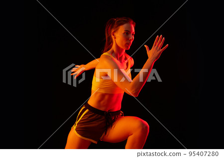 Dynamic portrait of young sportive woman training, running isolated on dark background in neon light. Competition, sport, fitness, speed and energy concept. Dynamic portrait of young sportive woman training, running isolated on dark background in neon light. Competition, sport, fitness, speed and energy concept. 95407280