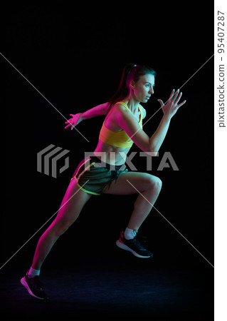 Professional female athlete running isolated on dark background in neon light. Healthy lifestyle, skills, sport, fitness, speed and energy concept. 95407287