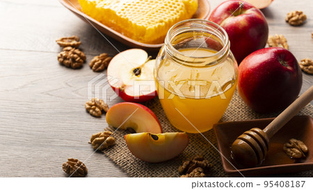 Mason jar with honey, honey dipper, honeycomb, red apples and walnuts on kitchen table 95408187