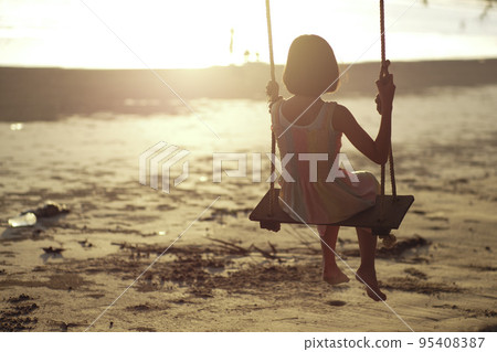 Rear view of lonely Asian girl sits on the wooden swing with sunset in background Rear view of lonely Asian girl sits on the wooden swing with sunset in background 95408387