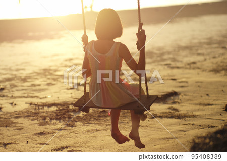 Rear view of lonely Asian girl sits on the wooden swing with sunset in background Rear view of lonely Asian girl sits on the wooden swing with sunset in background 95408389