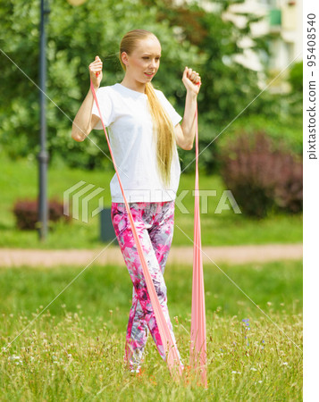 Girl doing exercises outdoor, using resistance fit band. Girl doing exercises outdoor, using resistance fit band. 95408540
