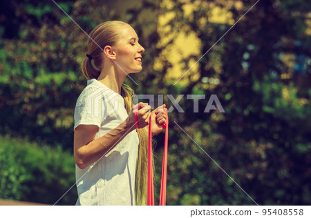 Girl doing exercises outdoor, using resistance fit band. 95408558