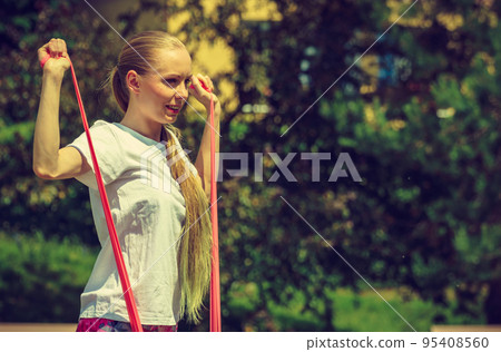 Girl doing exercises outdoor, using resistance fit band. 95408560