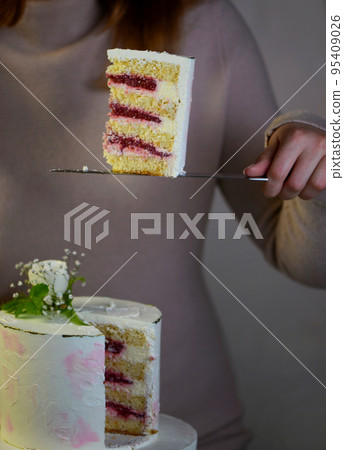 the girl cuts and serves a piece of cake. festive wedding two-tiered cake decorated with fresh flowers on a gray background the girl cuts and serves a piece of cake. festive wedding two-tiered cake decorated with fresh flowers on a gray background 95409026