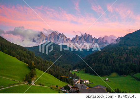 Val di Funes valley with amazing alpine Dolomites covered with pink clouds at sunset and Santa Maddalena village on the hill. Val di Funes valley with amazing alpine Dolomites covered with pink clouds at sunset and Santa Maddalena village on the hill. 95409143