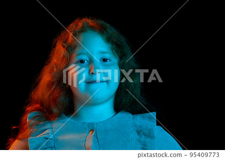 Charming redheaded little girl wearing festive dress looking at camera isolated over dark background in neon light. Kids emotions, facial expressions, fashion Charming redheaded little girl wearing festive dress looking at camera isolated over dark background in neon light. Kids emotions, facial expressions, fashion 95409773