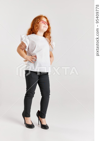 Little fashionista. Portrait of cute redheaded little girl wearing mother's heels isolated over white background. Kids emotions, facial expressions, fashion Little fashionista. Portrait of cute redheaded little girl wearing mother's heels isolated over white background. Kids emotions, facial expressions, fashion 95409778