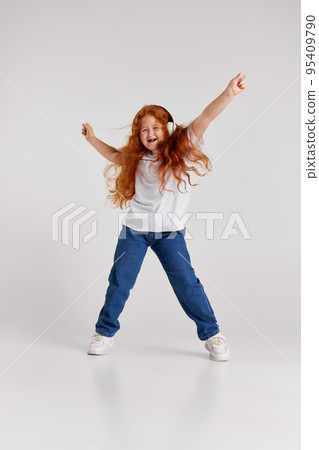 Joyful little girl, kid in white t-shirt and jeans listening to music and dancing isolated over white background. Kids fashion, emotions, carefree childhood Joyful little girl, kid in white t-shirt and jeans listening to music and dancing isolated over white background. Kids fashion, emotions, carefree childhood 95409790