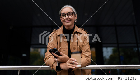 portrait of a stylish fifty year old businesswoman with a phone and a cup of coffee in her hands portrait of a stylish fifty year old businesswoman with a phone and a cup of coffee in her hands 95411283
