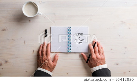 Top view of male hands in business suit placed next to an open notepad with Have a great day written in it Top view of male hands in business suit placed next to an open notepad with Have a great day written in it 95412080