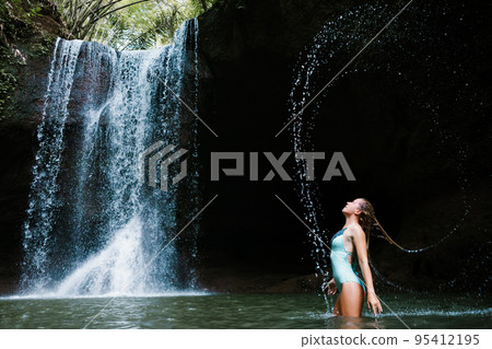 Woman have fun in natural pool under tropical waterfall 95412195