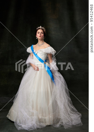 Young queen. Portrait of adorable girl in image of medieval royal person in renaissance style dress isolated on dark background. Comparison of eras, beauty, history, art Young queen. Portrait of adorable girl in image of medieval royal person in renaissance style dress isolated on dark background. Comparison of eras, beauty, history, art 95412468