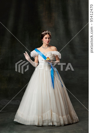 Young queen. Portrait of adorable girl in image of medieval royal person in renaissance style dress isolated on dark background. Comparison of eras, beauty, history, art 95412470