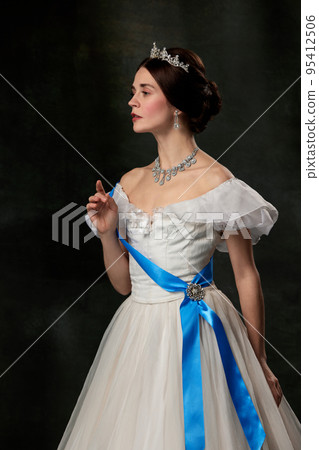 Young queen. Portrait of adorable girl in image of medieval royal person in renaissance style dress isolated on dark background. Comparison of eras, beauty, history, art 95412506