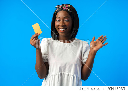 Young african woman holding credit card in hand against blue background Young african woman holding credit card in hand against blue background 95412685