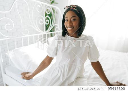 Beautiful young thoughtful african woman sitting in morning bed Beautiful young thoughtful african woman sitting in morning bed 95412800