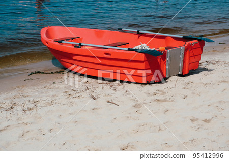 Plastic modern red life boat on the sandy beach of the river. Plastic modern red life boat on the sandy beach of the river. 95412996