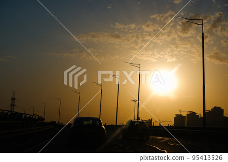 City landscape in the rays of the setting sun. Highways, cars, high-rise buildings and cranes in the light. Urban landscape 95413526