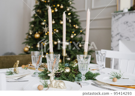 Beautiful glass glasses, candles in the decor of the festive table. Christmas table setting on the background of a Christmas tree Beautiful glass glasses, candles in the decor of the festive table. Christmas table setting on the background of a Christmas tree 95414293