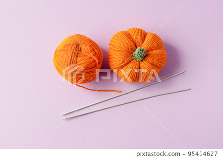 Knitted orange pumpkin and an orange ball of thread with knitting needles on a purple background, autumn composition, front view. Halloween concept. Knitted orange pumpkin and an orange ball of thread with knitting needles on a purple background, autumn composition, front view. Halloween concept. 95414627