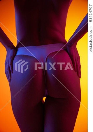 Cropped image of slim, smooth female body, buttocks in underwear isolated over orange background in neon light 95414707