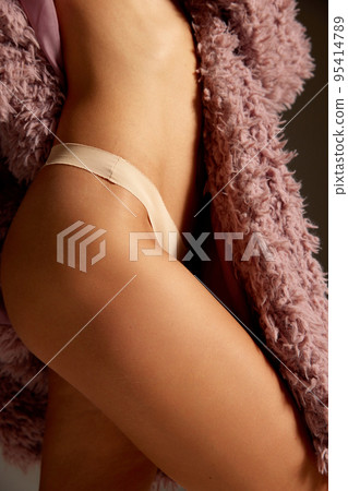 Cropped image of smooth, tanned female body, hip, legs. Woman posing in underwear and pink furry coat. No cellulite Cropped image of smooth, tanned female body, hip, legs. Woman posing in underwear and pink furry coat. No cellulite 95414789