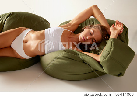 Portrait of beautiful woman lying on big pillows in white underwear isolated over grey background. Healthy sleep 95414806