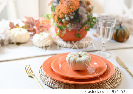 Thanksgiving day table setting with fall decorations, centerpiece of colorful flowers in pumpkin as vase. 95415263
