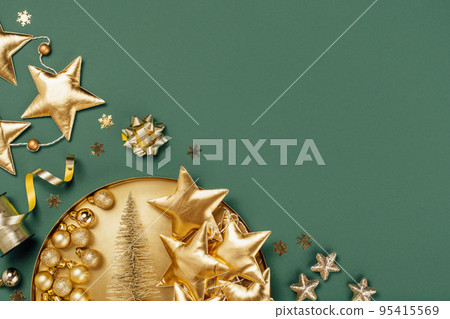 Merry Christmas and Happy New Year rich golden and crystal festive ornaments. stars glitter and Christmas tree on round golden tray plate on muted green. Party decor border. Top view 95415569