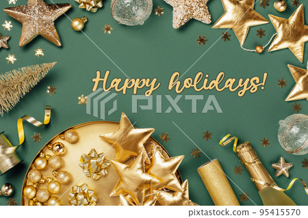 Happy holidays text card Merry Christmas and Happy New Year rich golden and crystal festive ornaments. stars glitter and Christmas tree on round golden tray plate on muted green. Party decor border. Happy holidays text card Merry Christmas and Happy New Year rich golden and crystal festive ornaments. stars glitter and Christmas tree on round golden tray plate on muted green. Party decor border. 95415570