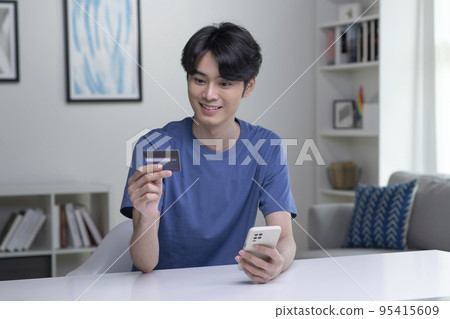 Asian man holding credit card and using smartphone. Businessman working at home. Online shopping Asian man holding credit card and using smartphone. Businessman working at home. Online shopping 95415609
