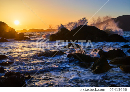 Waves crashing over boulders on ocean during sunset Waves crashing over boulders on ocean during sunset 95415666