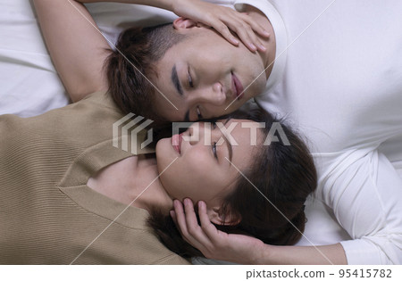 Asian couples lie on the bed, faces close to each other in love Asian couples lie on the bed, faces close to each other in love 95415782