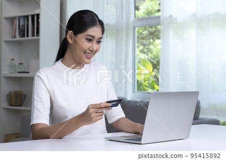 Asian woman holding credit card and using laptop computer Asian woman holding credit card and using laptop computer 95415892