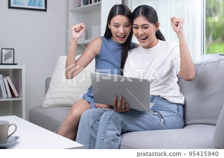 Asian lesbian couple using laptop in the living room. happily raising their hands up Asian lesbian couple using laptop in the living room. happily raising their hands up 95415940