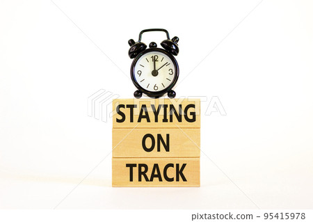Staying on track symbol. Concept words Staying on track on wooden blocks on a beautiful white table white background. Black alarm clock. Business, motivational and staying on track concept. Staying on track symbol. Concept words Staying on track on wooden blocks on a beautiful white table white background. Black alarm clock. Business, motivational and staying on track concept. 95415978