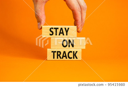 Stay on track symbol. Concept words Stay on track on wooden blocks on a beautiful orange table orange background. Businessman hand. Business, motivational and stay on track concept. Copy space. Stay on track symbol. Concept words Stay on track on wooden blocks on a beautiful orange table orange background. Businessman hand. Business, motivational and stay on track concept. Copy space. 95415980
