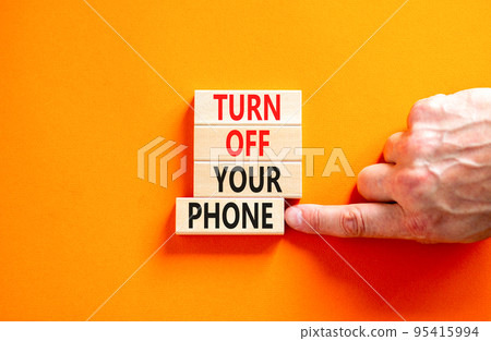 Turn off your phone symbol. Concept words Turn off your phone on wooden blocks. Beautiful orange background. Businessman hand. Business psychological turn off your phone concept. Copy space Turn off your phone symbol. Concept words Turn off your phone on wooden blocks. Beautiful orange background. Businessman hand. Business psychological turn off your phone concept. Copy space 95415994