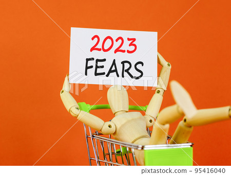 2023 Fears symbol. White paper with words 2023 Fears, human model in shopcart. Beautiful orange table orange background. Business and 2023 fears concept. Copy space. 95416040