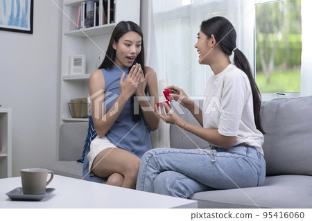 Surprised young woman with raising her hands and smiling while her girlfriend proposing her  95416060