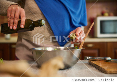 Close-up. Selective focus. Unrecognizable woman, housewife in a blue hijab, pours olive oil into a bowl with fresh healthy raw vegan vegetable salad. Cooking. Cookery. Healthy eating. Vegetarianism Close-up. Selective focus. Unrecognizable woman, housewife in a blue hijab, pours olive oil into a bowl with fresh healthy raw vegan vegetable salad. Cooking. Cookery. Healthy eating. Vegetarianism 95416212
