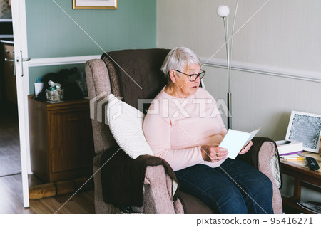 Grey hair senior woman in eyeglasses reading a book and smiling while resting on the armchair in living room at home, Pleasant retired female enjoying interesting life in retirement. Selective focus. Grey hair senior woman in eyeglasses reading a book and smiling while resting on the armchair in living room at home, Pleasant retired female enjoying interesting life in retirement. Selective focus. 95416271