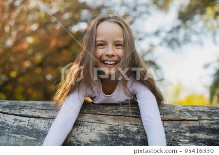 A cute little girl lies on a fallen log in the park. 95416330