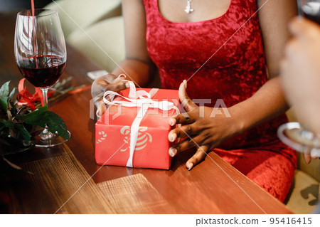 Midsection of a couple enjoying day out at restaurant. Black man and woman drinking wine. Focus on a woman's hands holding a gift box. Midsection of a couple enjoying day out at restaurant. Black man and woman drinking wine. Focus on a woman's hands holding a gift box. 95416415