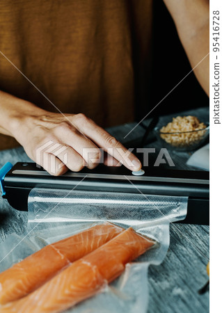 man vacuum-packing two pieces of salmon 95416728