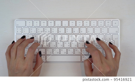 A young girl is typing on a wireless keyboard. Girl's hands close up. View from above. A young girl is typing on a wireless keyboard. Girl's hands close up. View from above. 95416921