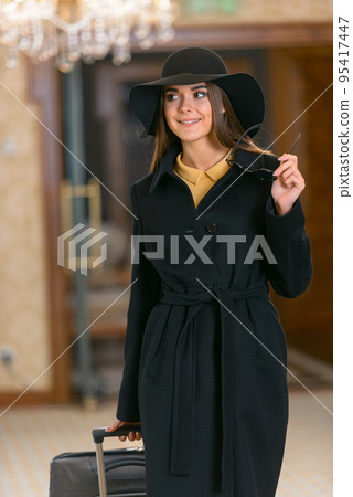 Happy young woman in hat with travel bag walking inside hotel 95417447