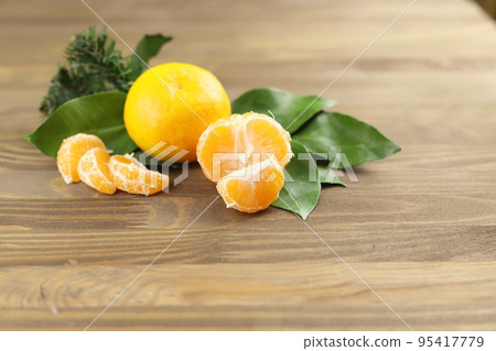 Mandarin or tangerine fruits whole and sliced, green leaves , fir tree on wooden background Mandarin or tangerine fruits whole and sliced, green leaves , fir tree on wooden background 95417779